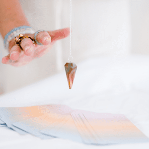 Oracle cards on a table with therapist using a pendulum – intuitive energy reading and holistic guidance session