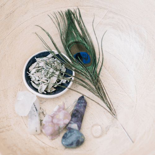 Crystals, dried sage, and a peacock feather arranged on a healing altar for energy clearing and holistic therapy