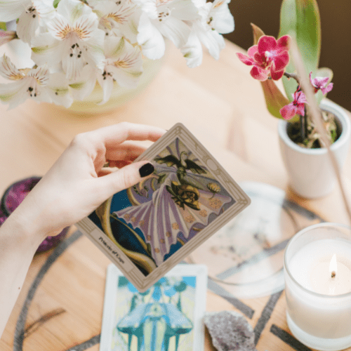 Therapist holding an oracle card with candle and flowers – intuitive healing and spiritual guidance sessio
