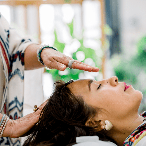 Reiki healing session – therapist channeling energy with hands above a fully clothed woman lying on a treatment bed